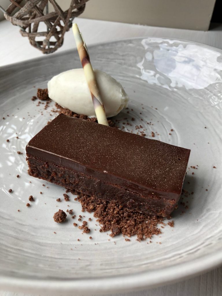 a picture of our chocolate delice cake. topped with some edible glitter and a scoop of vanilla ice cream behind with a chocolate crumb along the bottom  